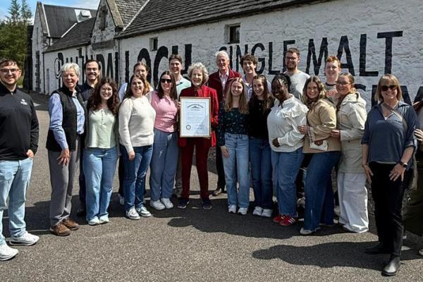 Group poses in front of distillery in Scotland