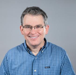 Man in blue shirt smiles to camera with gray background